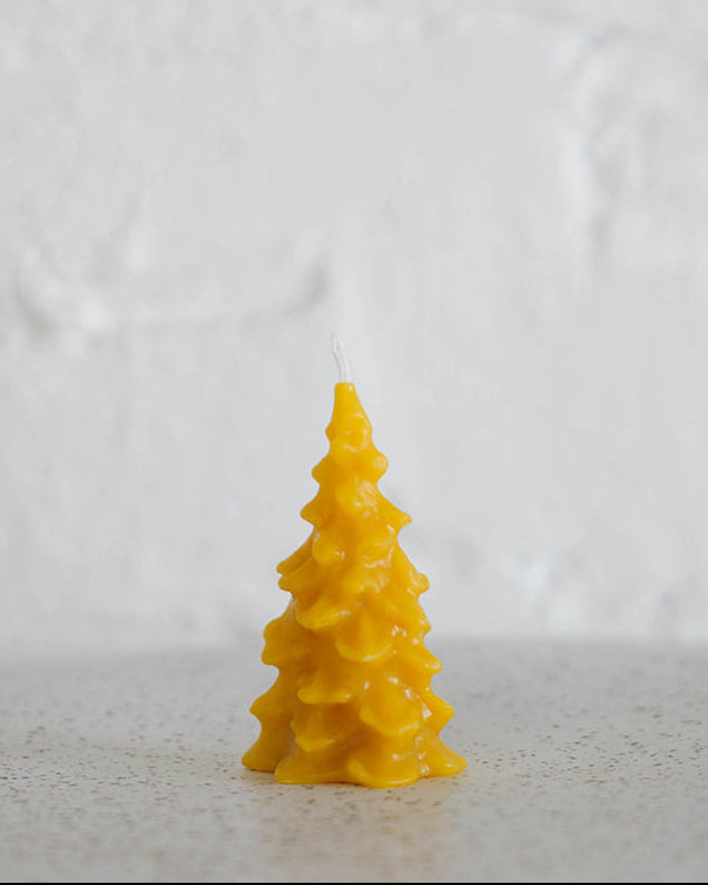 Pine tree shaped yellow candle on a textured white background