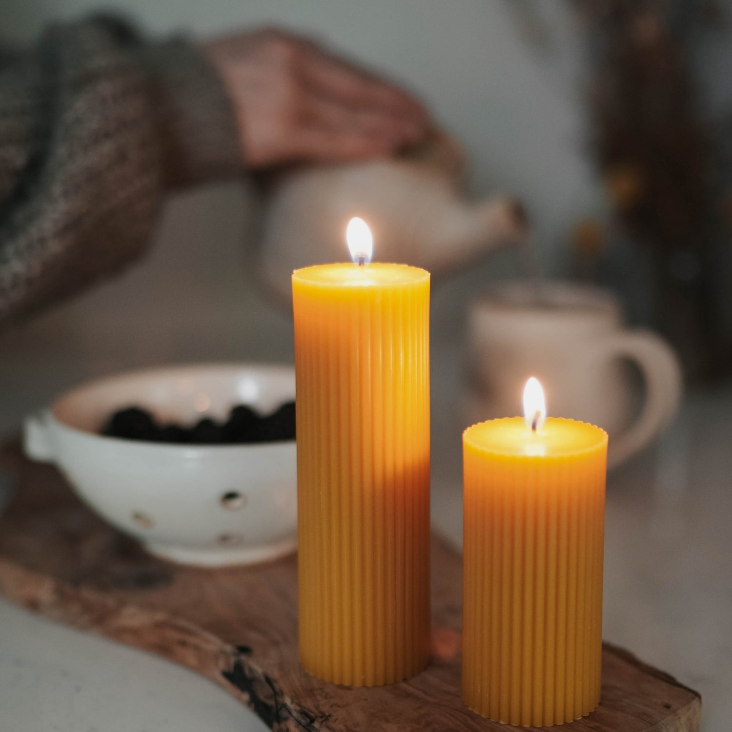 Beeswax candles burning while a person pours tea in the background.