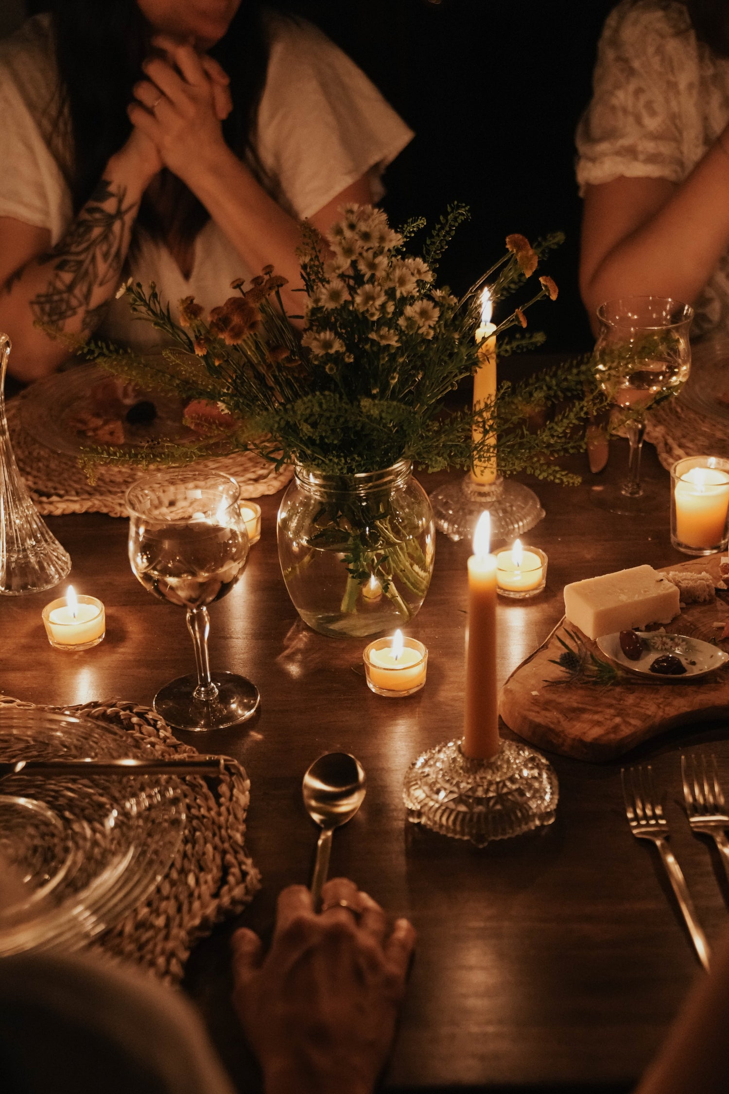 Beeswax taper candles glow on a dining table surrounded by women.